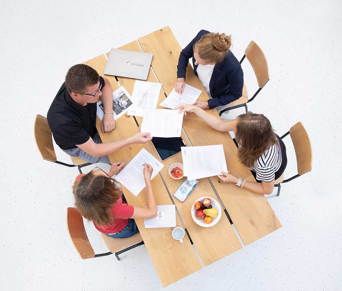 Sicht von oben: vier Menschen sitzen mit Unterlagen an einem Tisch