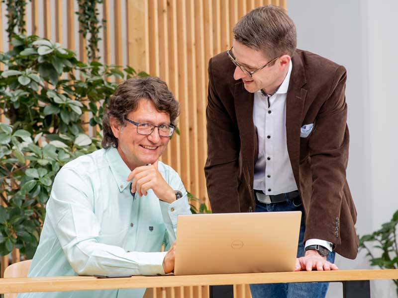 Zwei Männer schauen auf einen Monitor und besprechen ein Software-Einführungsprojekt.